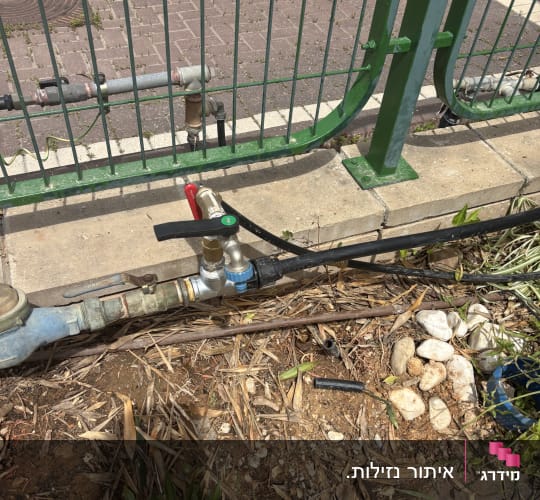 צינור מים ושסתום ליד גדר ירוקה